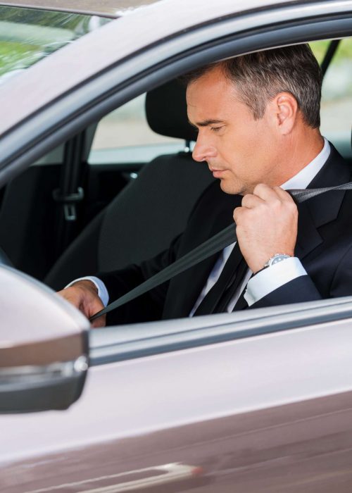 Fastening his seat belt. Confident mature businessman fastening seat belt while sitting in his car